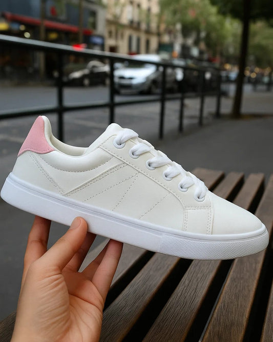 White sneaker with pink heel being held on a wooden bench with a city street background