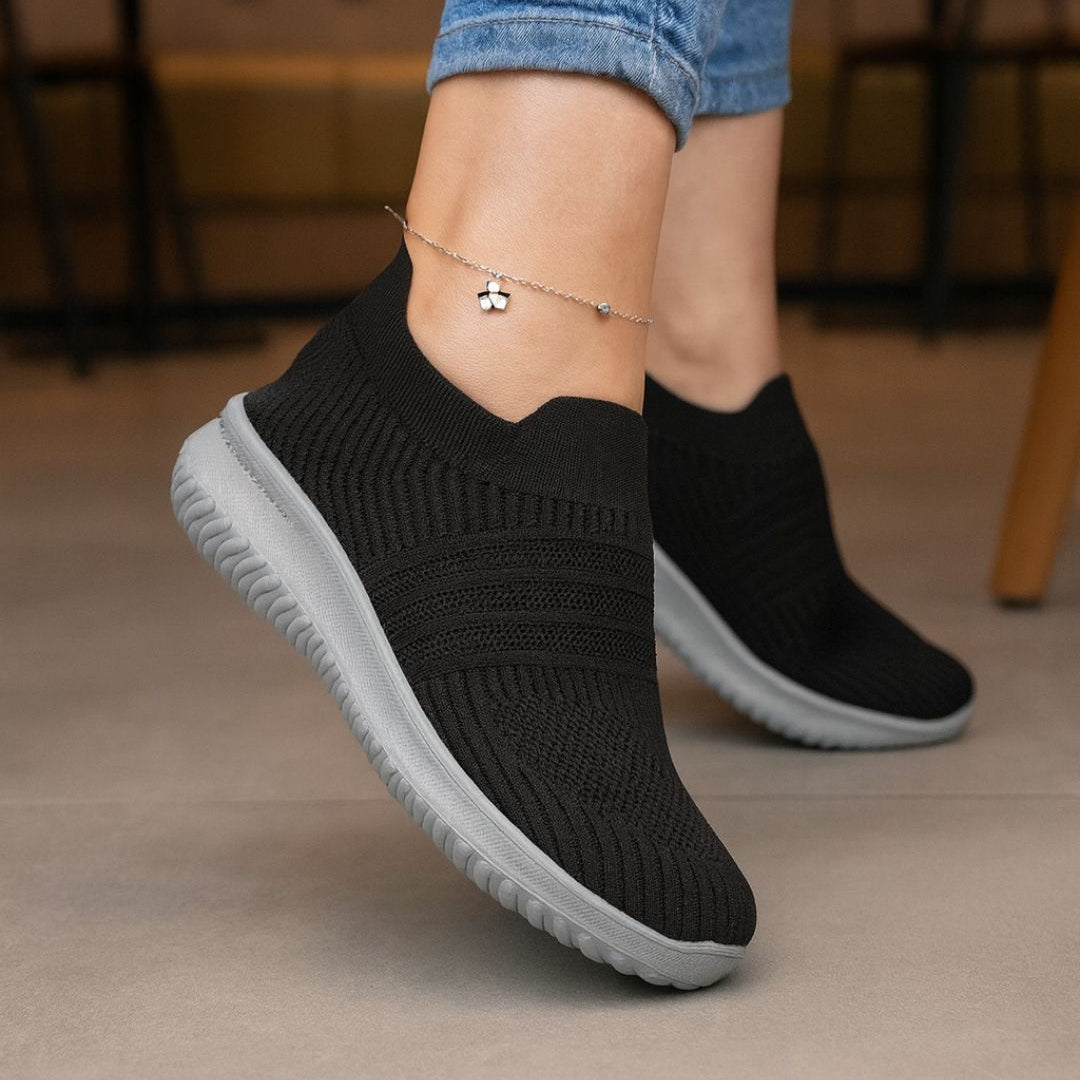 Black slip-on sneakers with gray soles worn indoors.