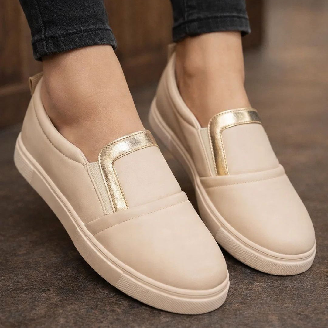 Beige slip-on shoes with gold accents worn indoors on a blurred background