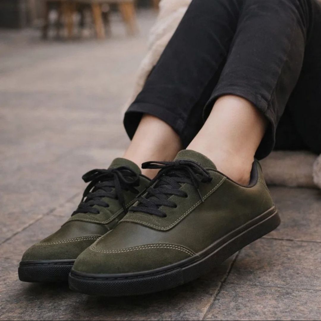 Green sneakers worn with black pants on a stone pavement.