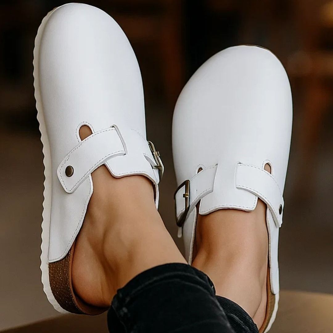 White clogs with brown soles worn by a person on a blurred background