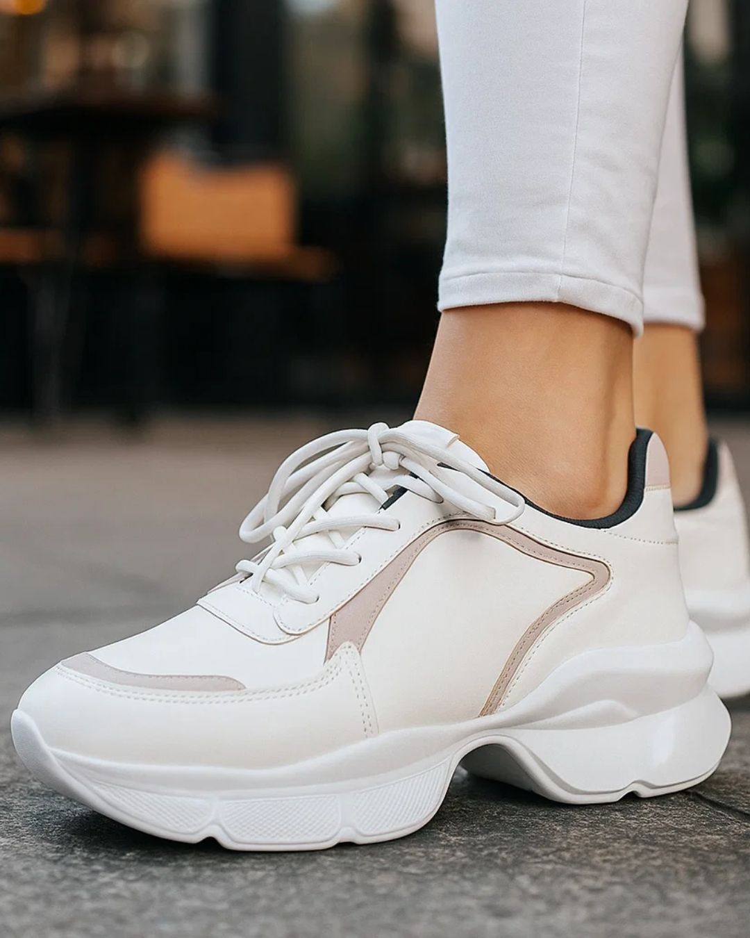 White sneakers with a thick sole worn by a person on a blurred background