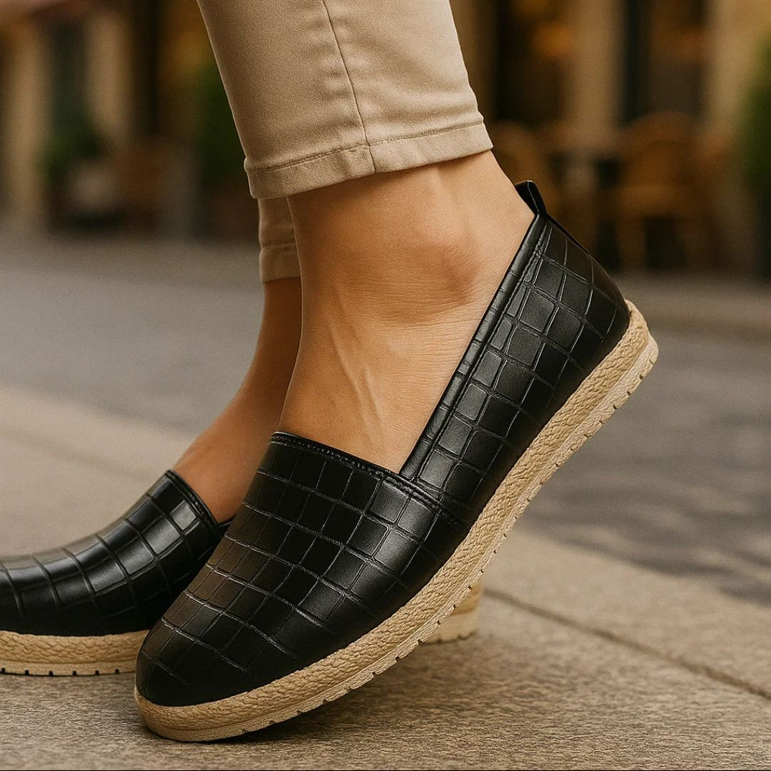 Black crocodile-patterned loafers with jute soles worn by a person on a blurred street background