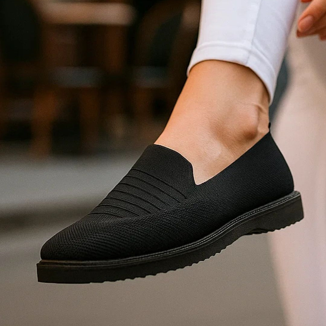 Black slip-on shoes worn with white pants in an outdoor setting