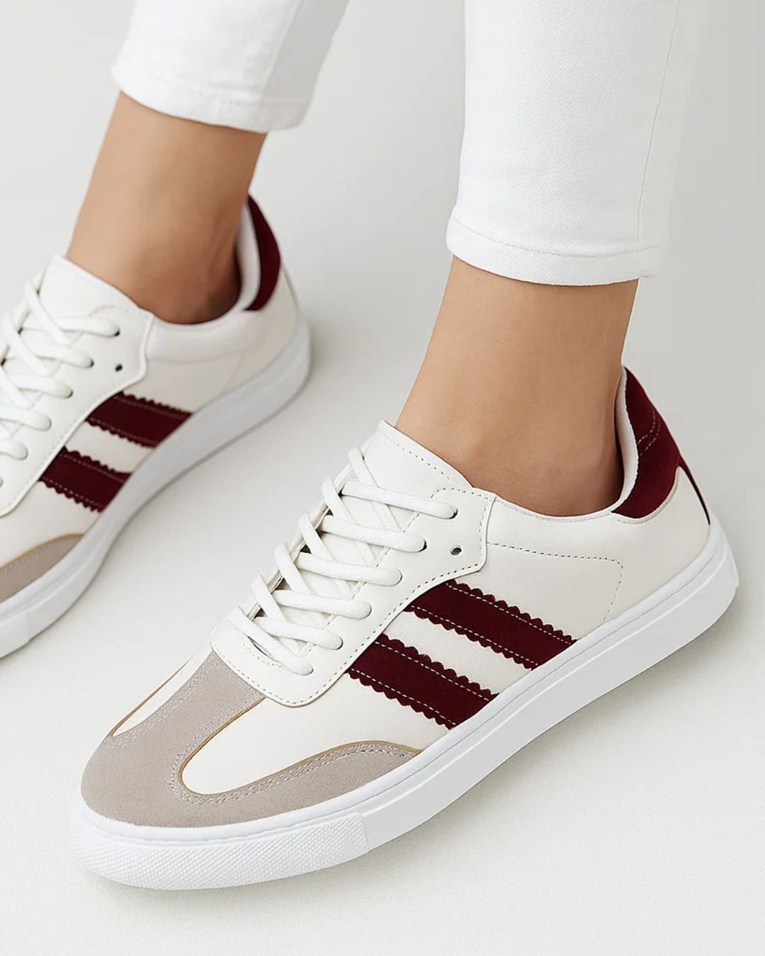 White sneakers with maroon stripes worn by a person on a white background