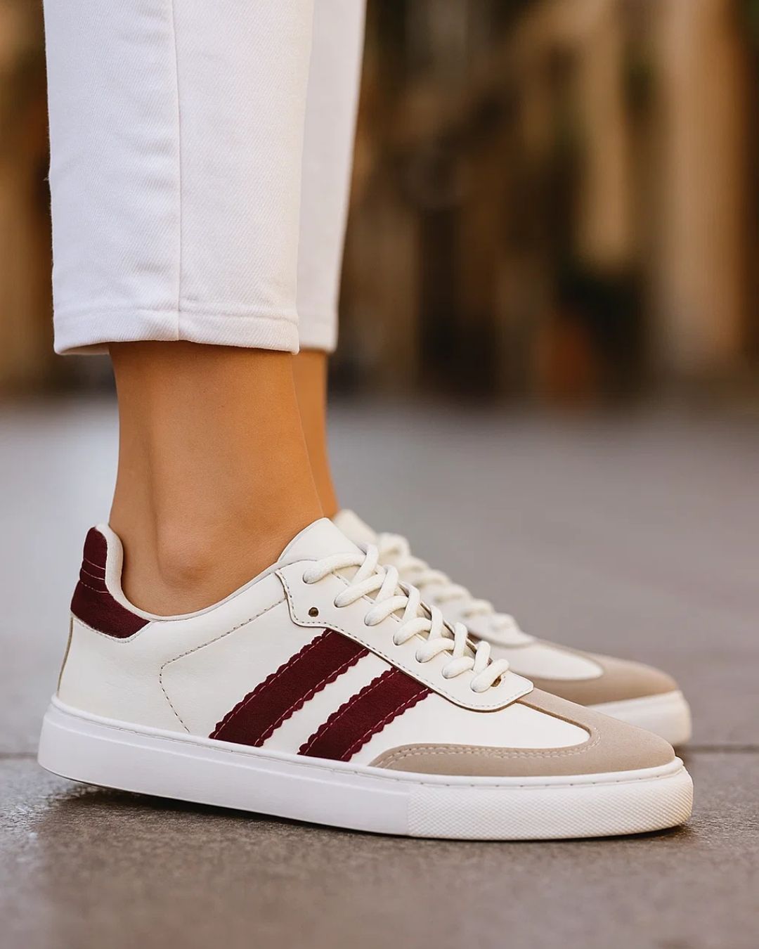 White sneakers with maroon stripes worn by a person on a blurred background