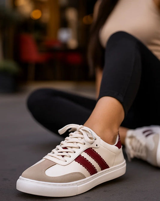 White sneakers with red stripes worn by a person sitting on the floor.