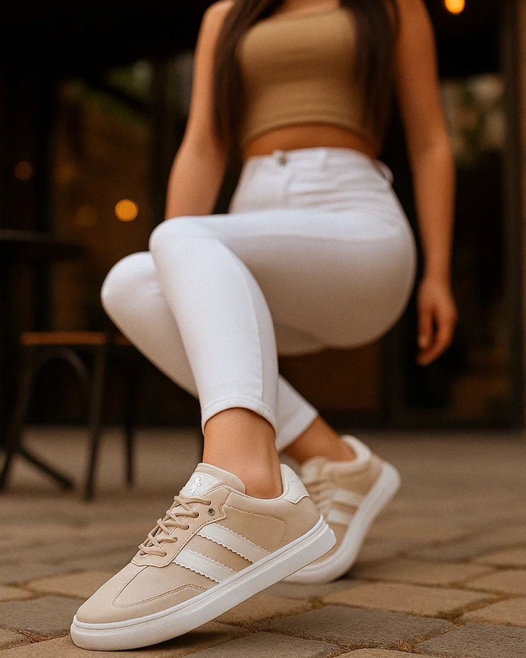 Person wearing beige sneakers with white stripes sitting on a stone pavement.