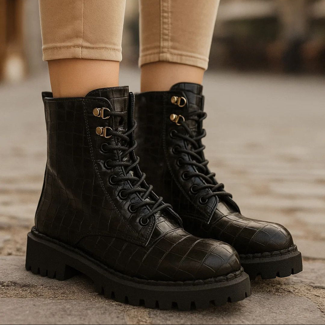 Black lace-up boots worn with beige pants on a blurred background