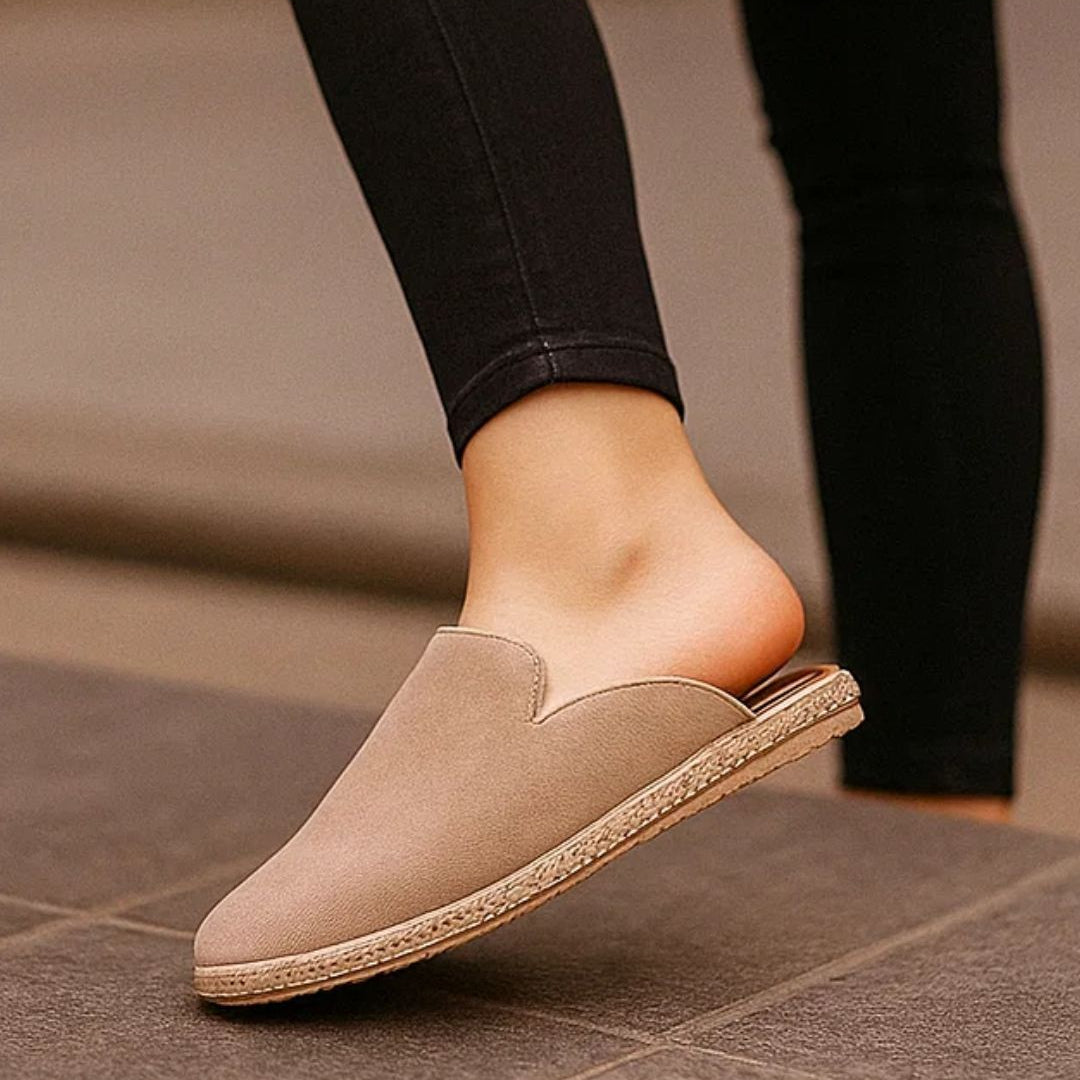 Beige slip-on shoe worn with black pants on a tiled floor.