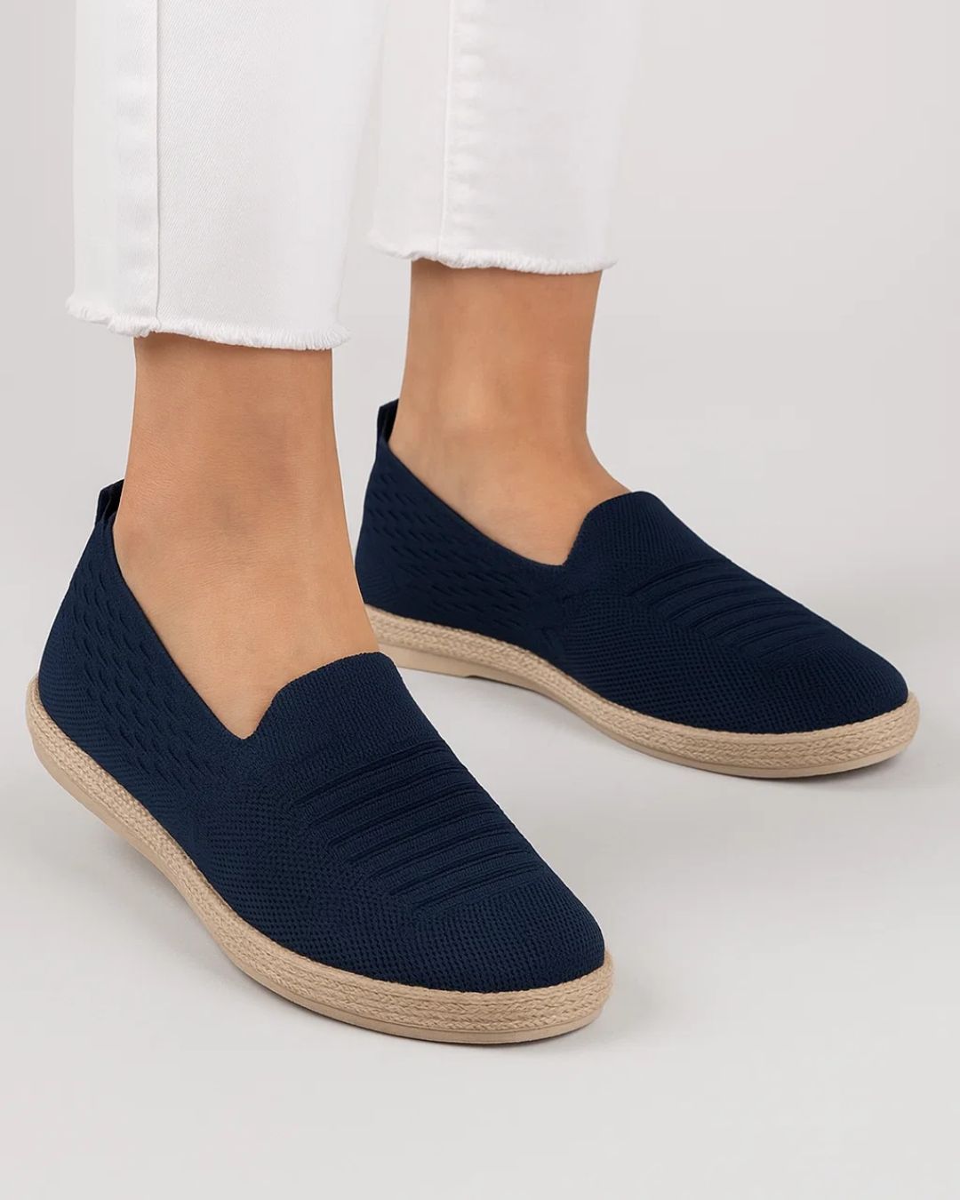 Navy slip-on shoes with beige soles worn by a person on a light gray background