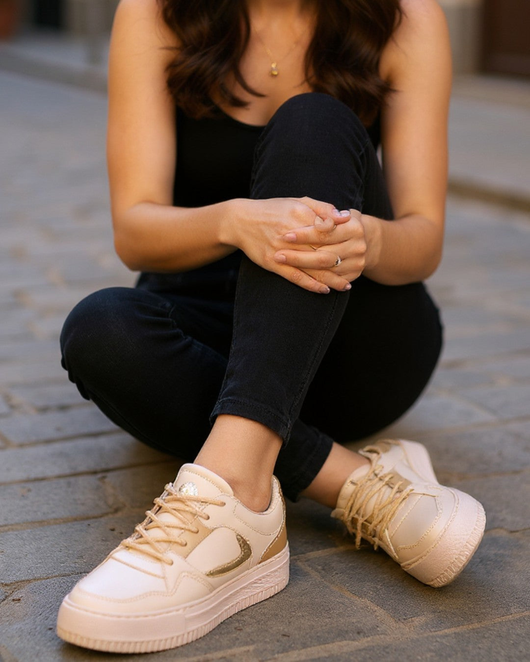 Person wearing beige sneakers sitting on a stone pavement