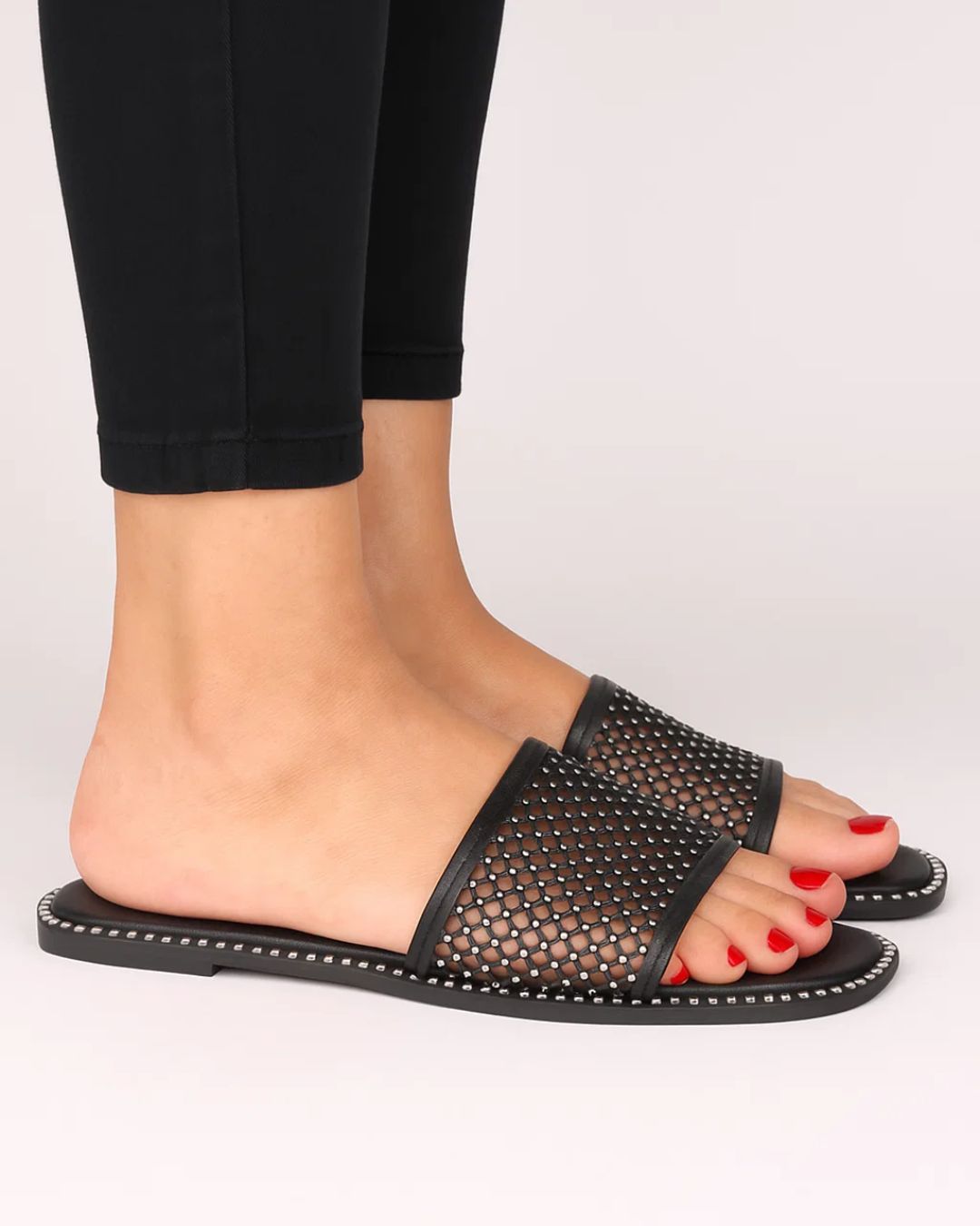 Black mesh sandals worn with black pants on a light gray background