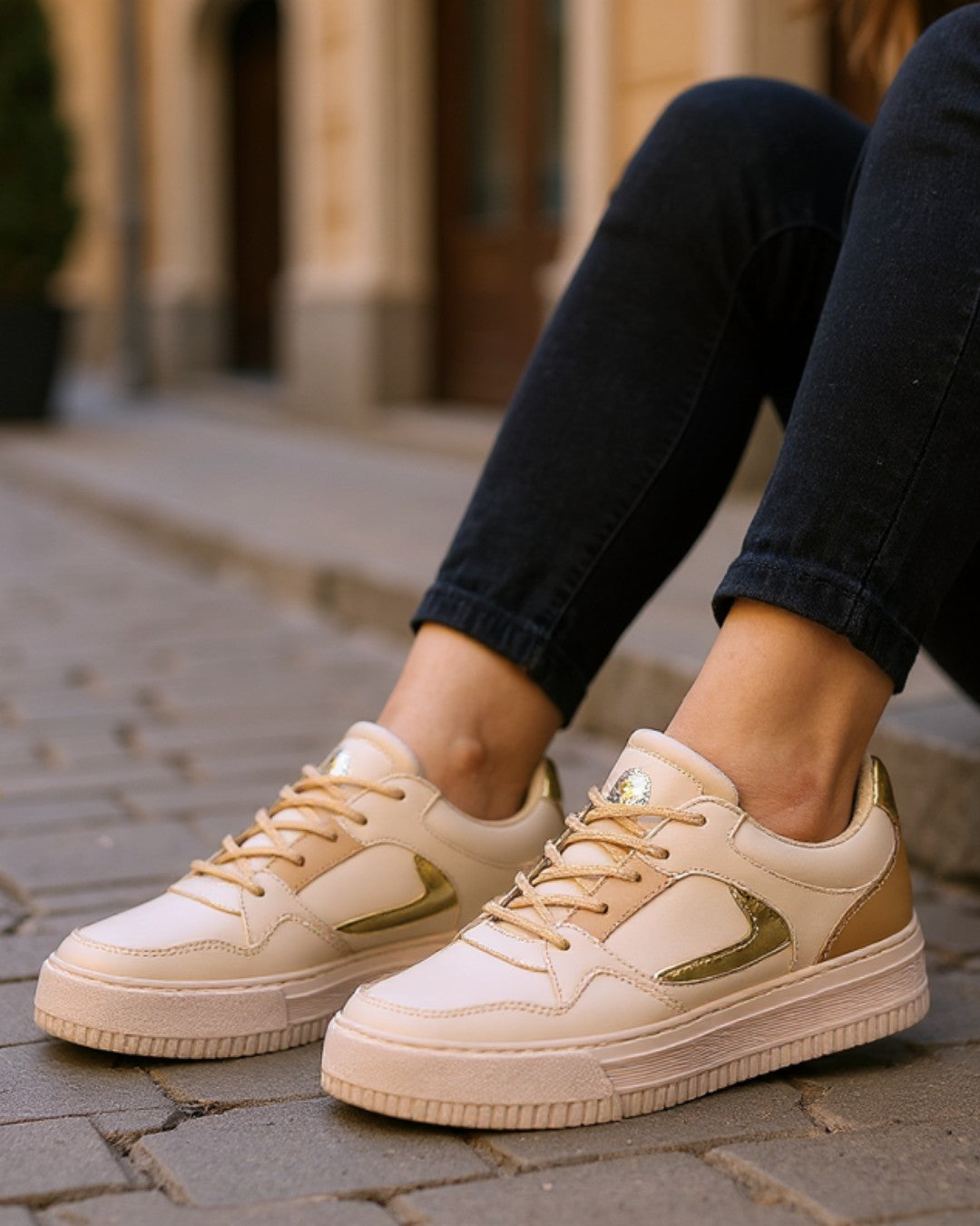 Beige sneakers with gold accents worn on a stone pavement.
