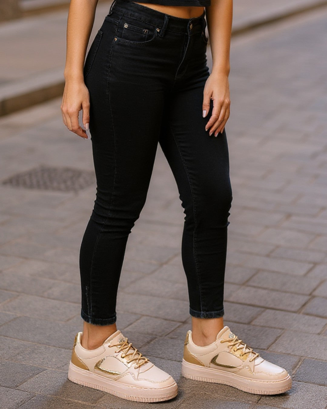 Person wearing black jeans and beige sneakers on a paved street