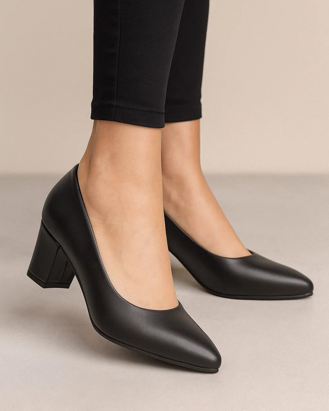 Black high-heeled shoes worn with black pants on a neutral background