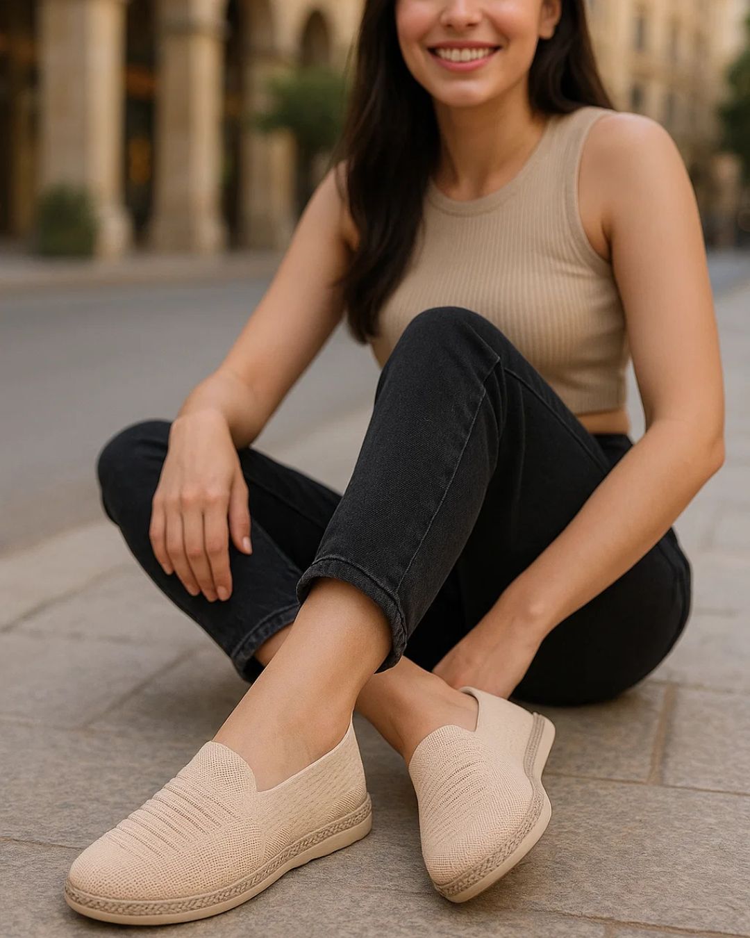 Woman sitting on a street wearing beige espadrilles and black pants.