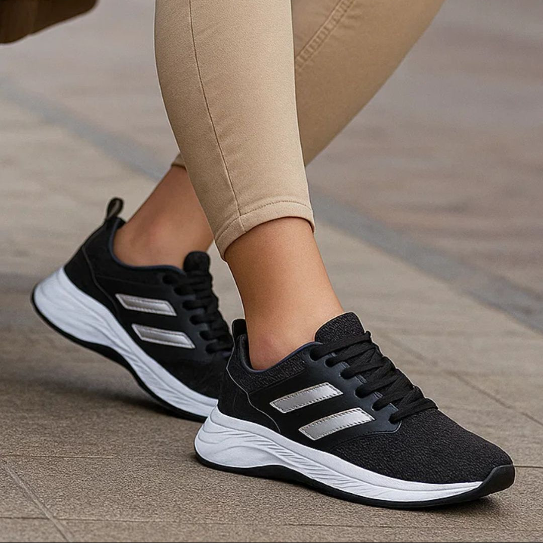 Person wearing black Adidas sneakers with white soles on a blurred outdoor background