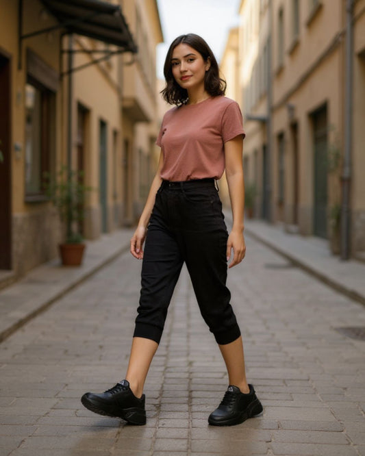 Woman in a pink shirt and black pants standing on a street.