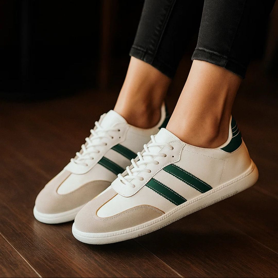 White sneakers with green stripes worn by a person on a wooden floor.