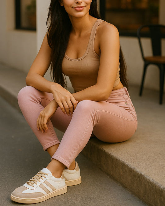 Woman sitting on steps wearing a beige tank top and pink pants with white sneakers.