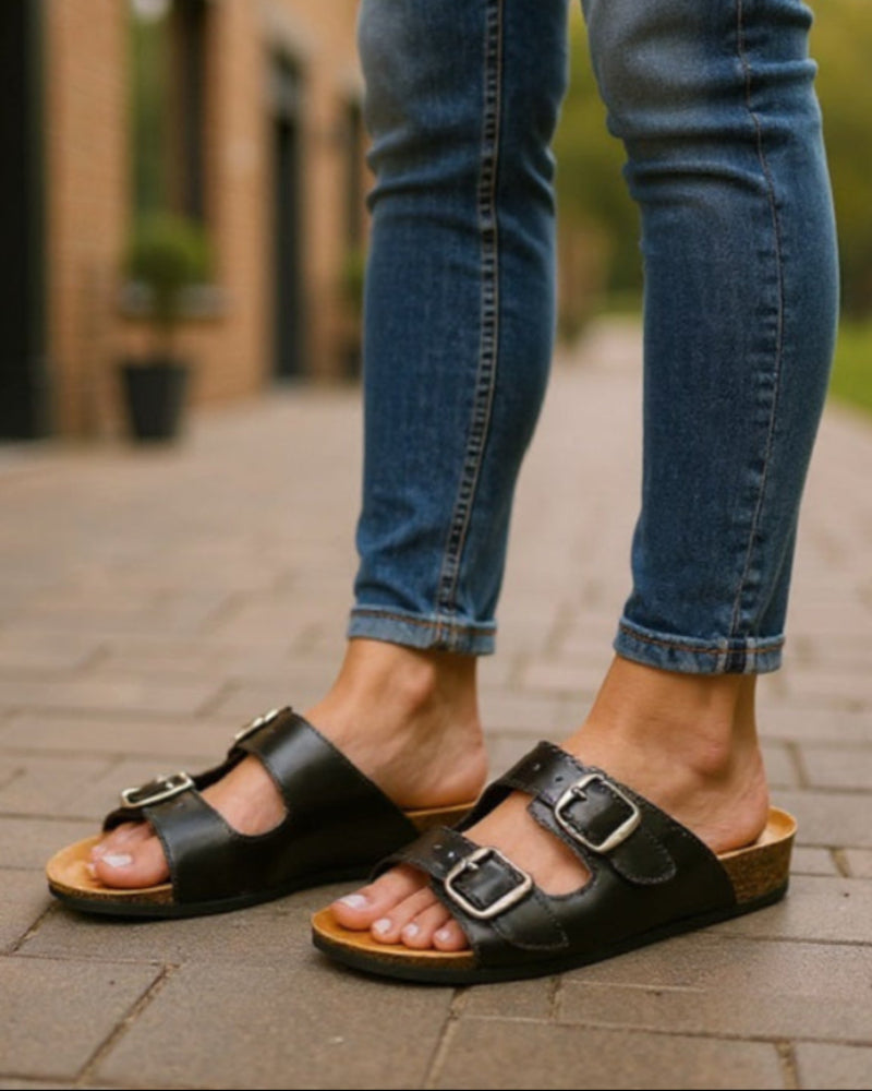 Person wearing black sandals and blue jeans on a paved walkway.