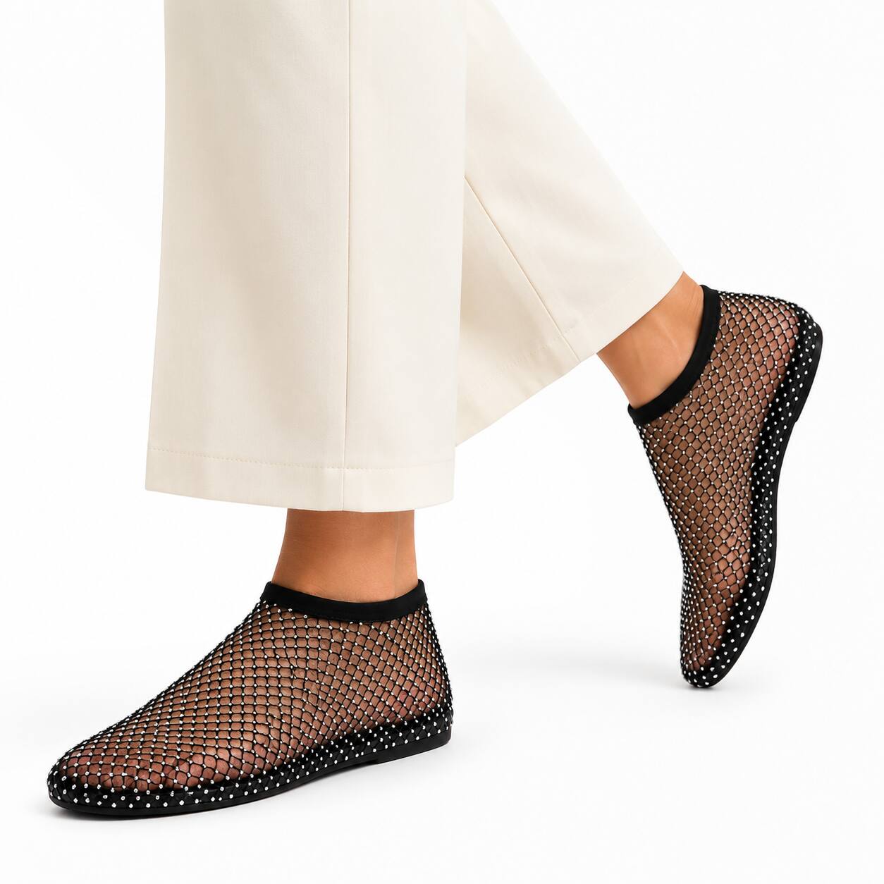 Black mesh slip-on socks with black trim, shown on a model wearing off-white trousers against a clean white background.