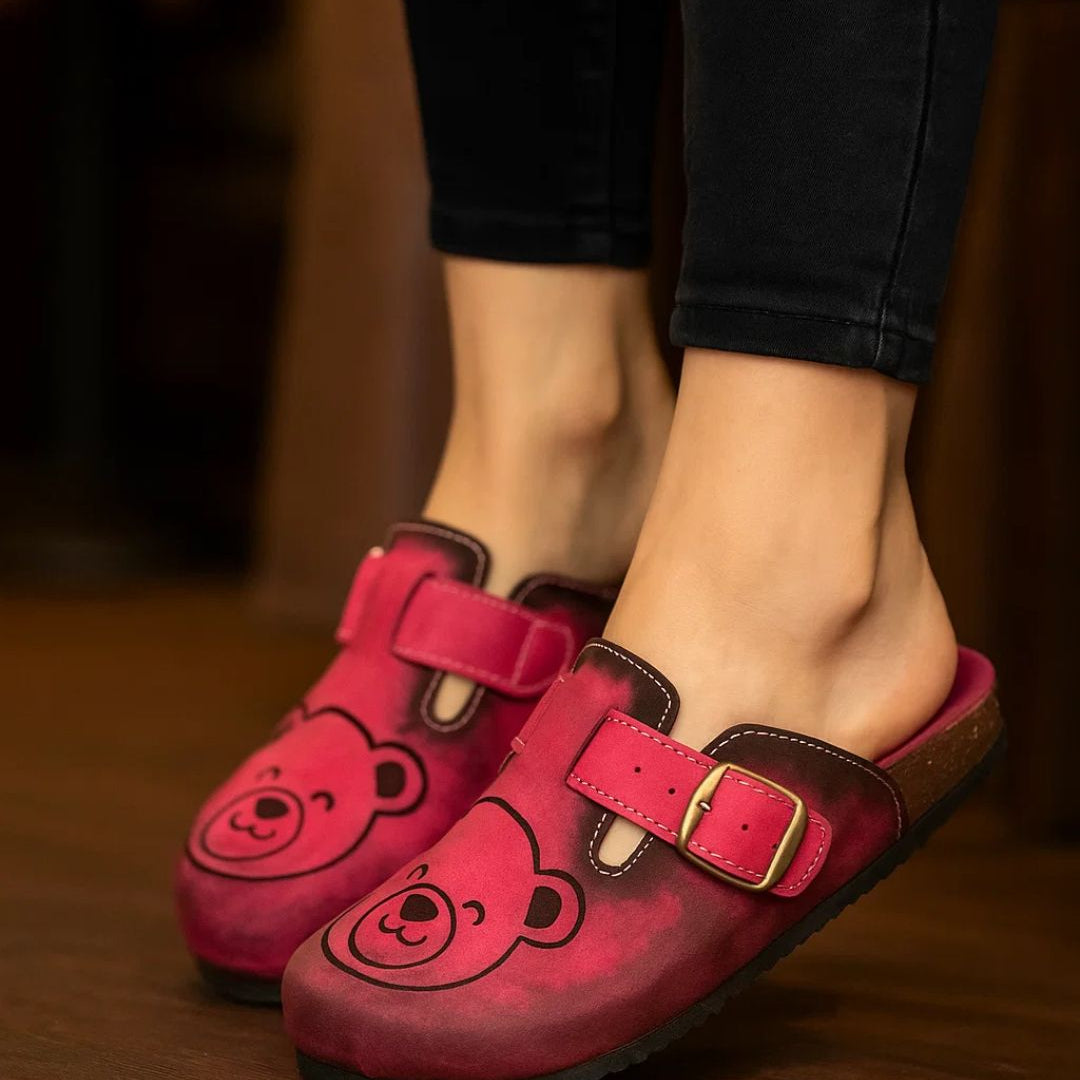 Red children's clogs with bear face design worn indoors.