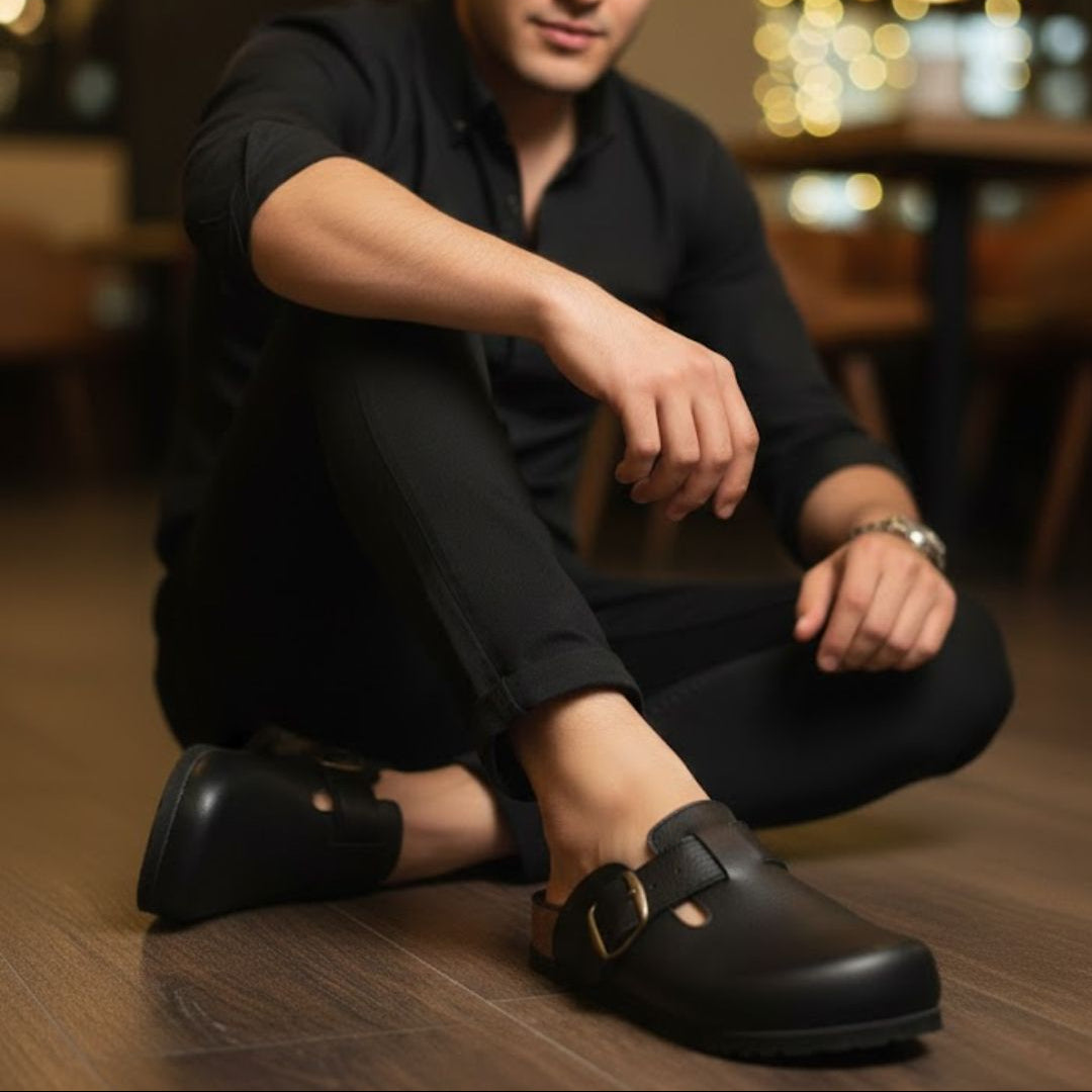 Man wearing black shoes sitting on a wooden floor with blurred lights in the background
