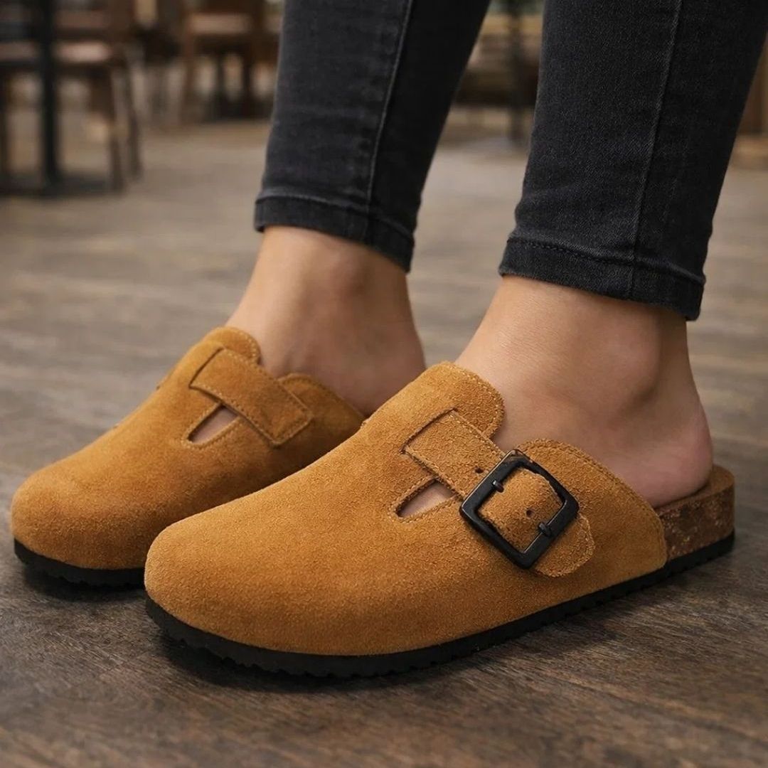 Brown suede clogs with a buckle on a wooden floor.