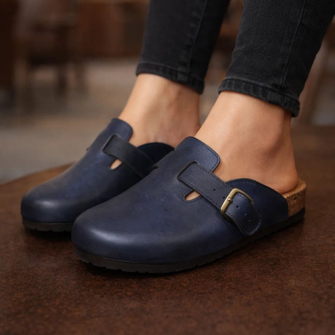 Navy blue clogs worn with black jeans on a blurred indoor background