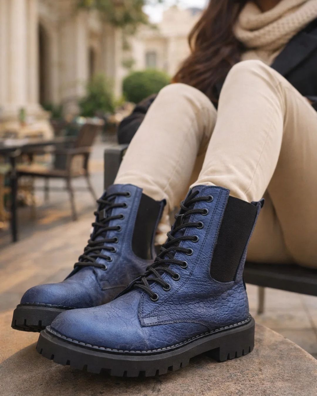 Blue leather boots with black soles worn by a person sitting outdoors.