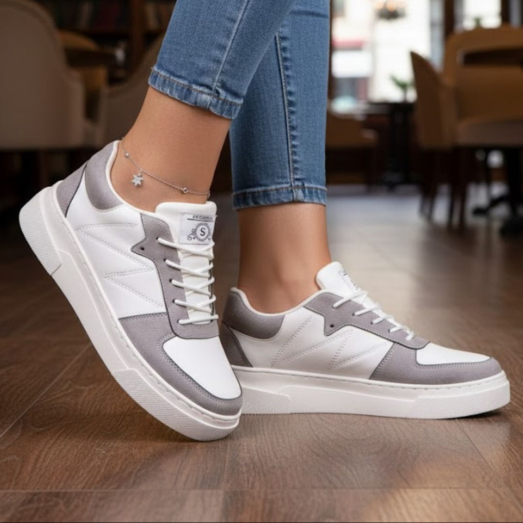 White and gray sneakers worn with blue jeans on a wooden floor.