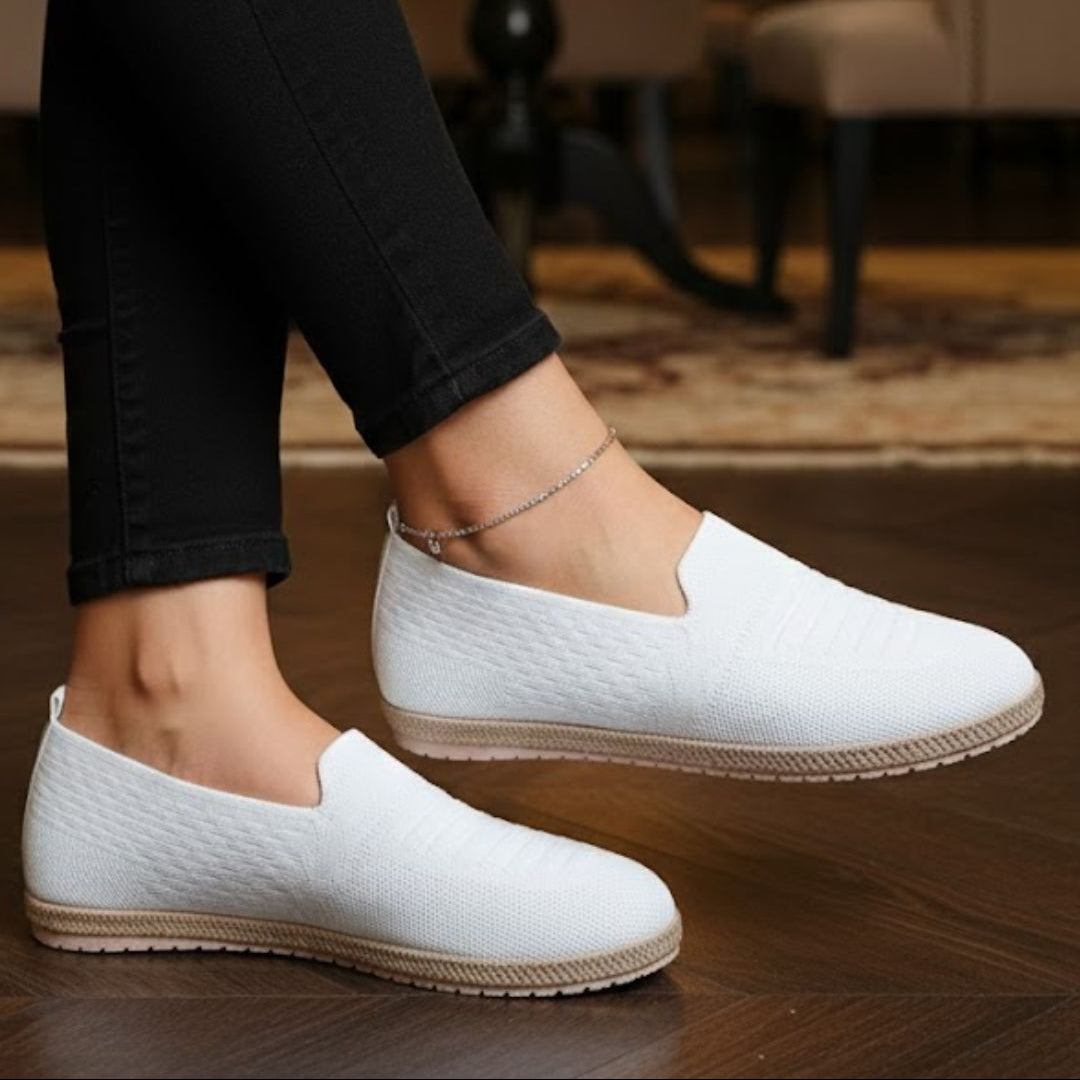 White loafers worn with black pants on a wooden floor.