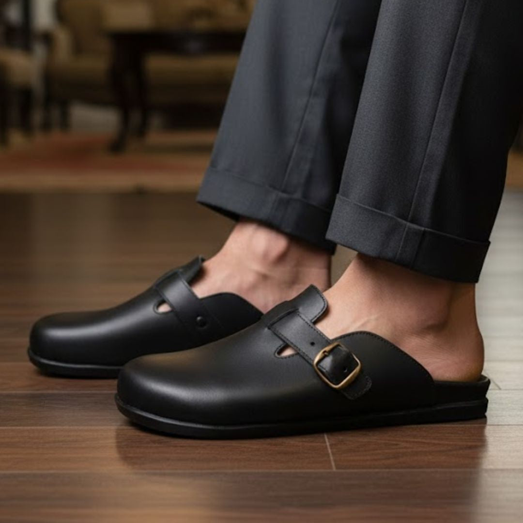 Black leather shoes with buckles worn indoors on a wooden floor.