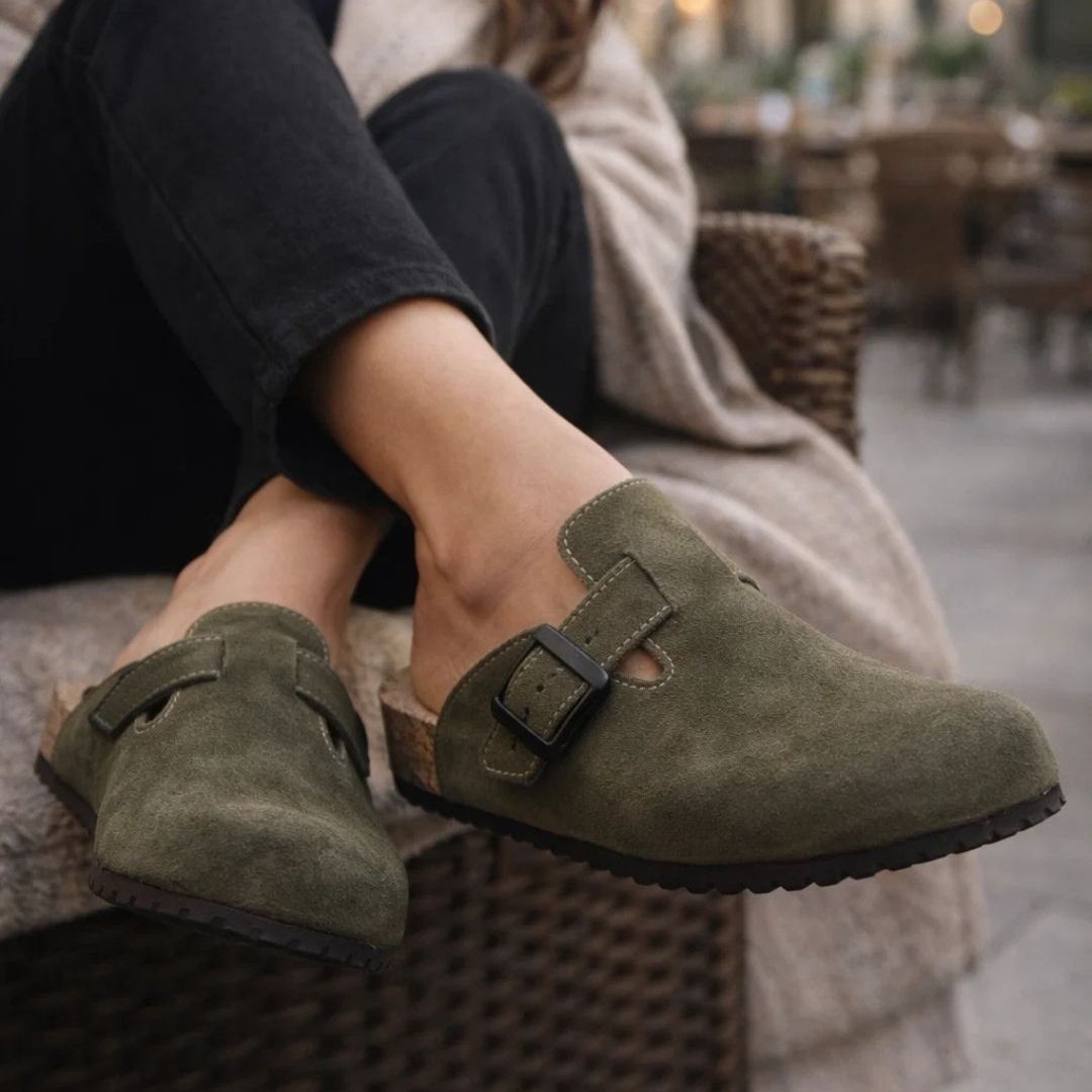 Green suede shoes with buckles worn by a person sitting outdoors.