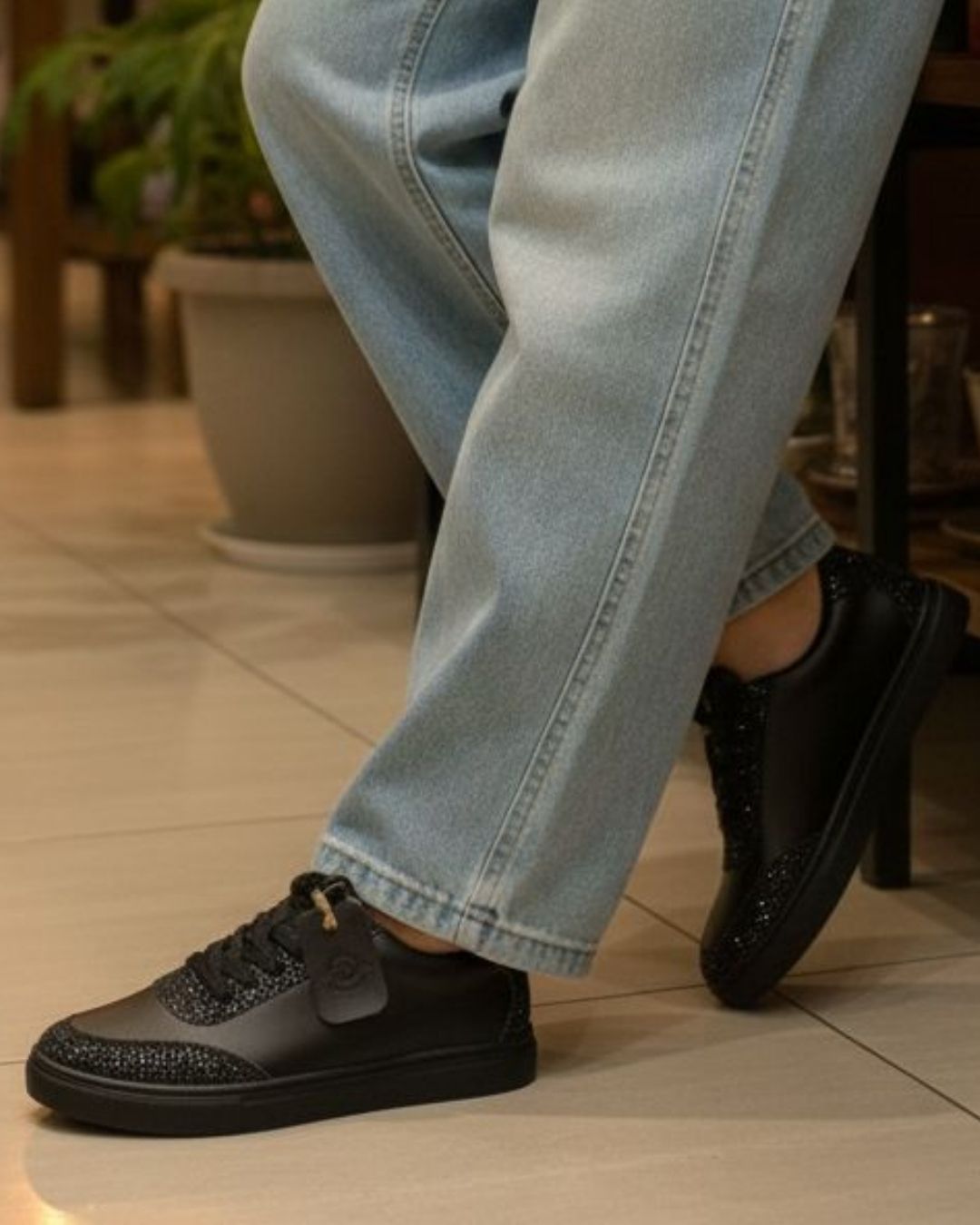 Person wearing black shoes and light blue jeans on a tiled floor.