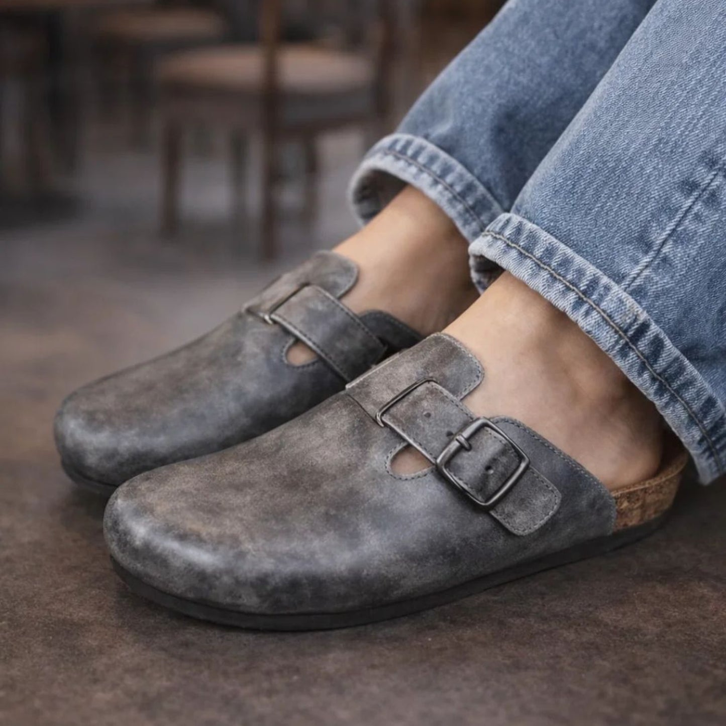 Gray suede shoes with buckles worn by a person in a casual setting.