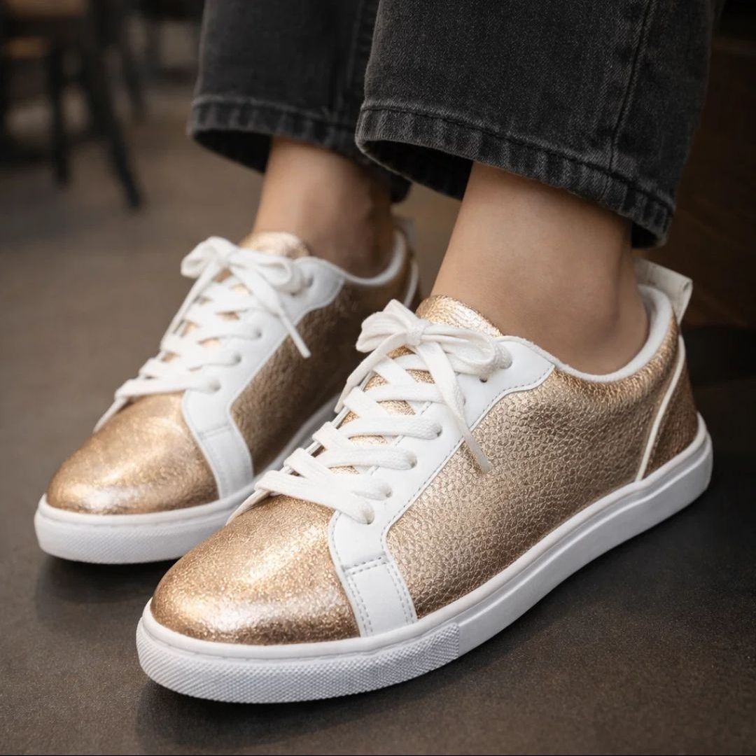 Gold and white sneakers worn with dark jeans on a blurred background