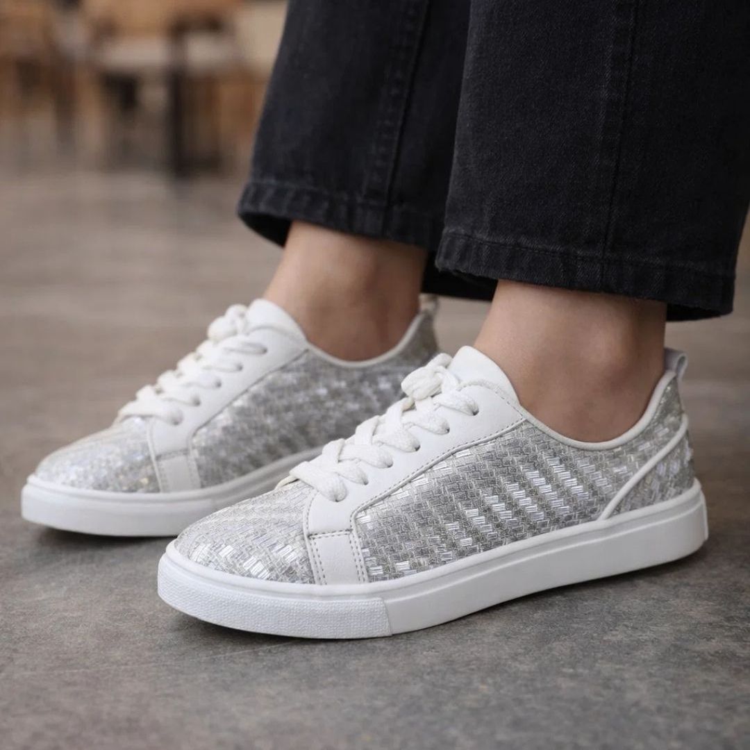 White sneakers with glittery side panels worn by a person on a blurred background