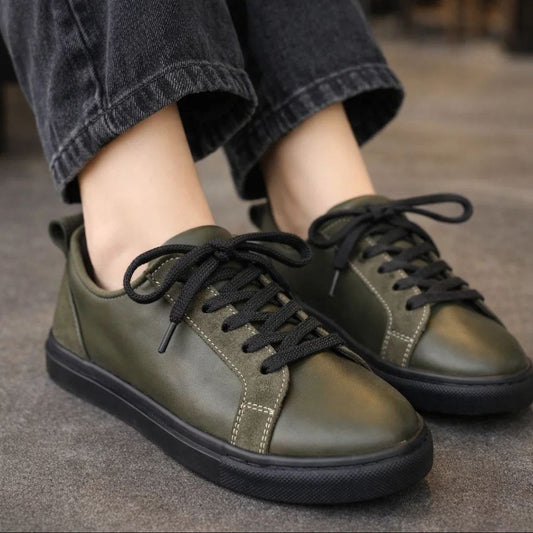 Green sneakers with black laces worn by a person on a gray surface