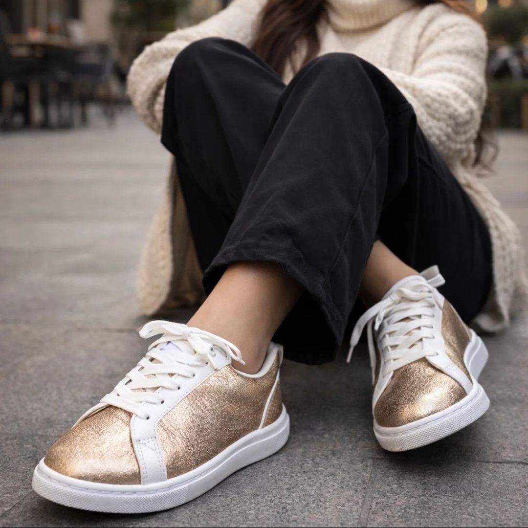 Person wearing gold glittery sneakers with white soles on a blurred outdoor background