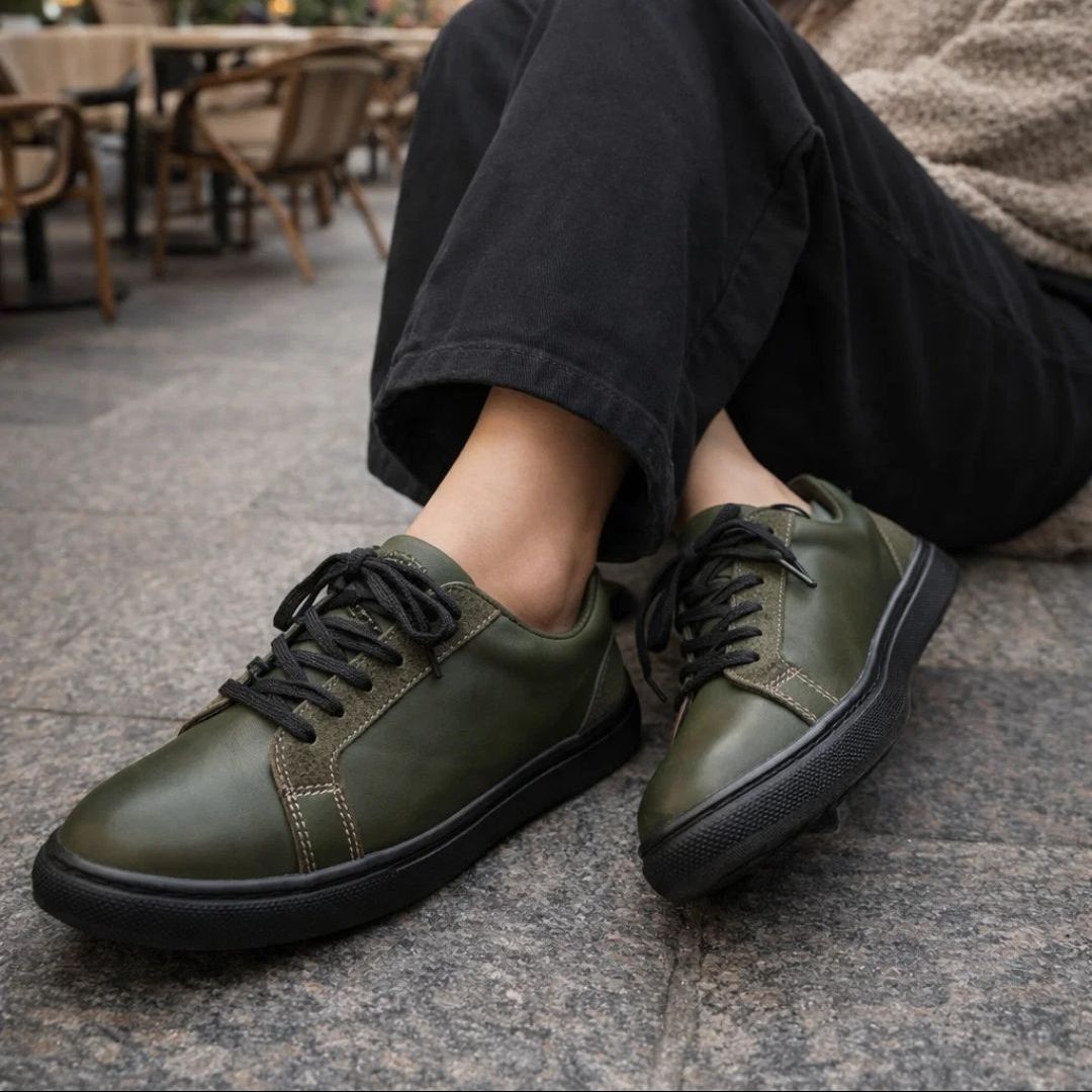Green leather shoes with black laces worn by a person sitting on a stone surface.