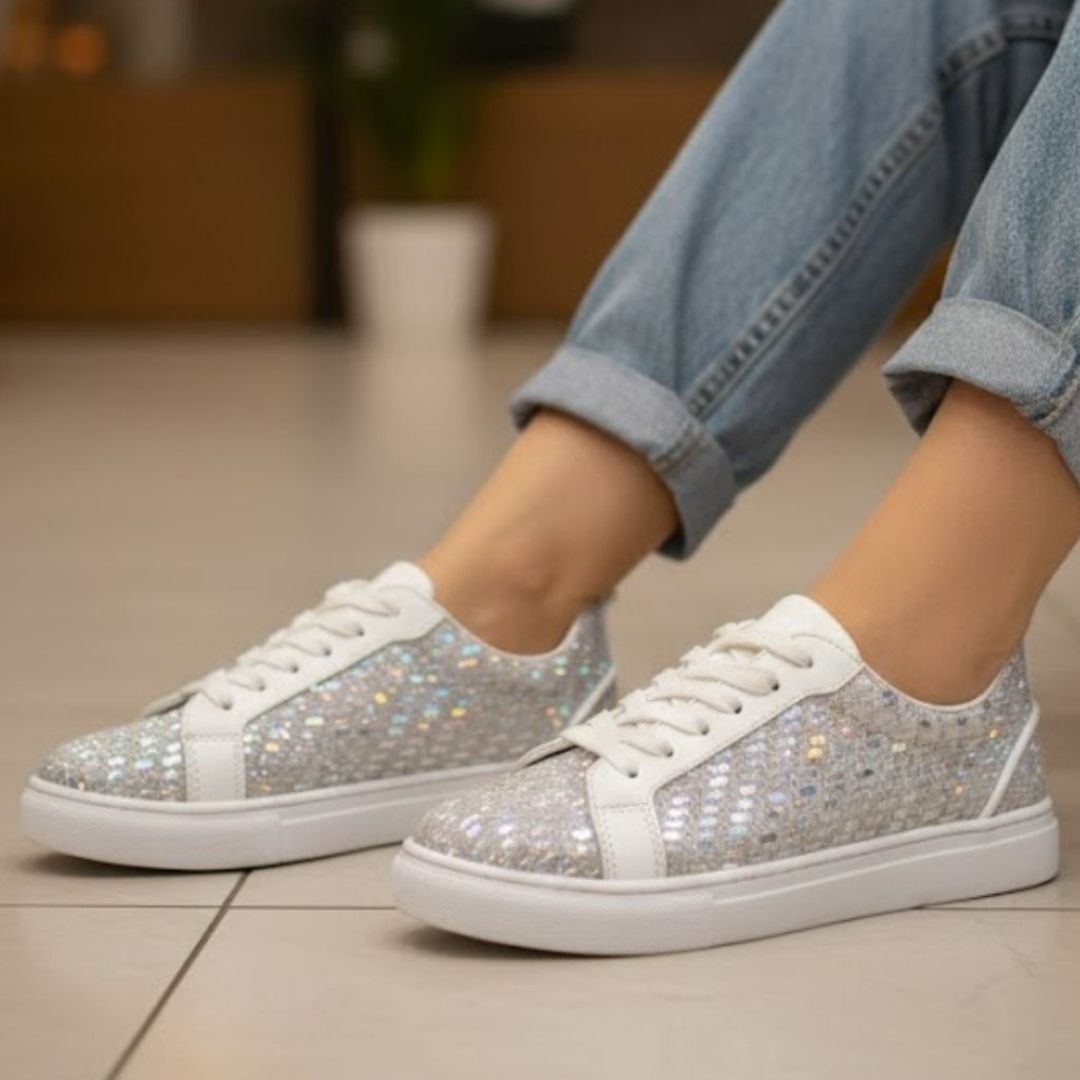 Silver glitter sneakers worn with light blue jeans on a neutral background
