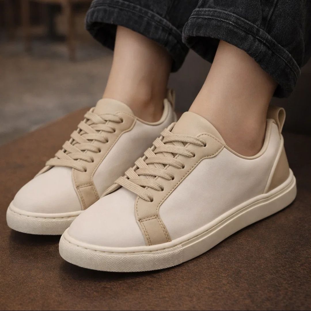 Beige sneakers worn with dark jeans on a brown surface