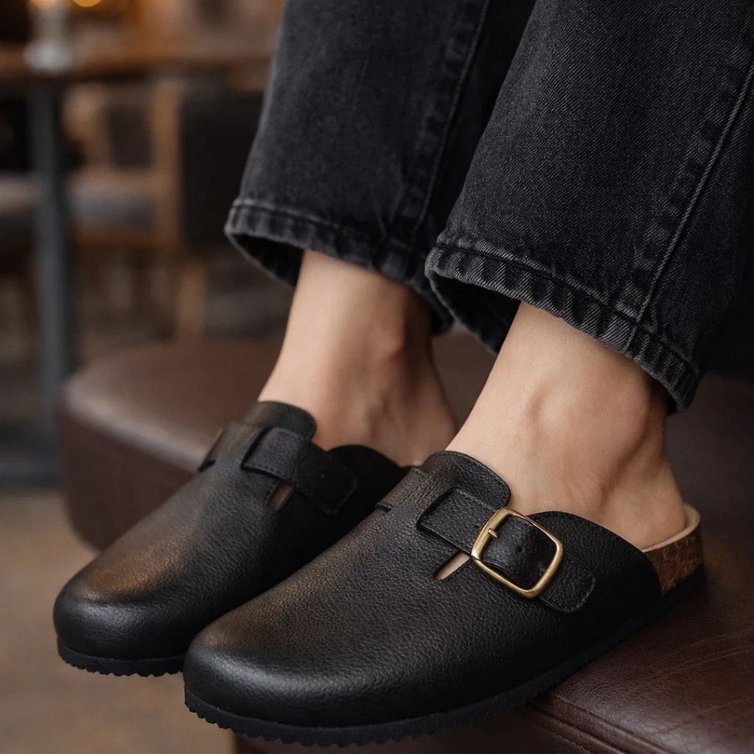 Black leather clogs with a gold buckle worn indoors.