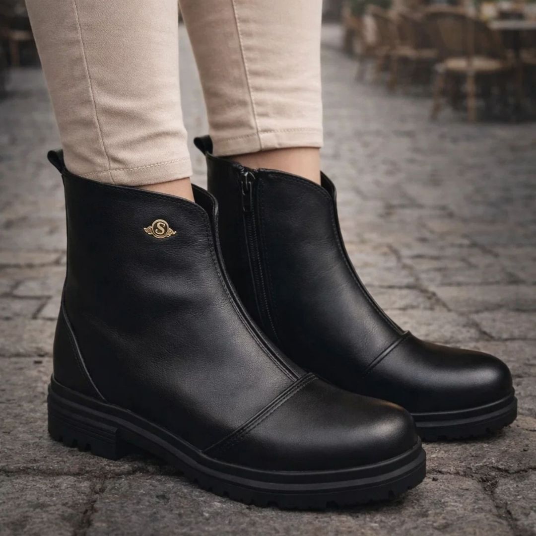 Black ankle boots worn on a stone pavement with a blurred outdoor background