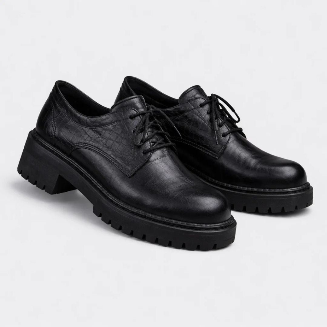 Pair of black leather shoes with thick soles on a light gray background