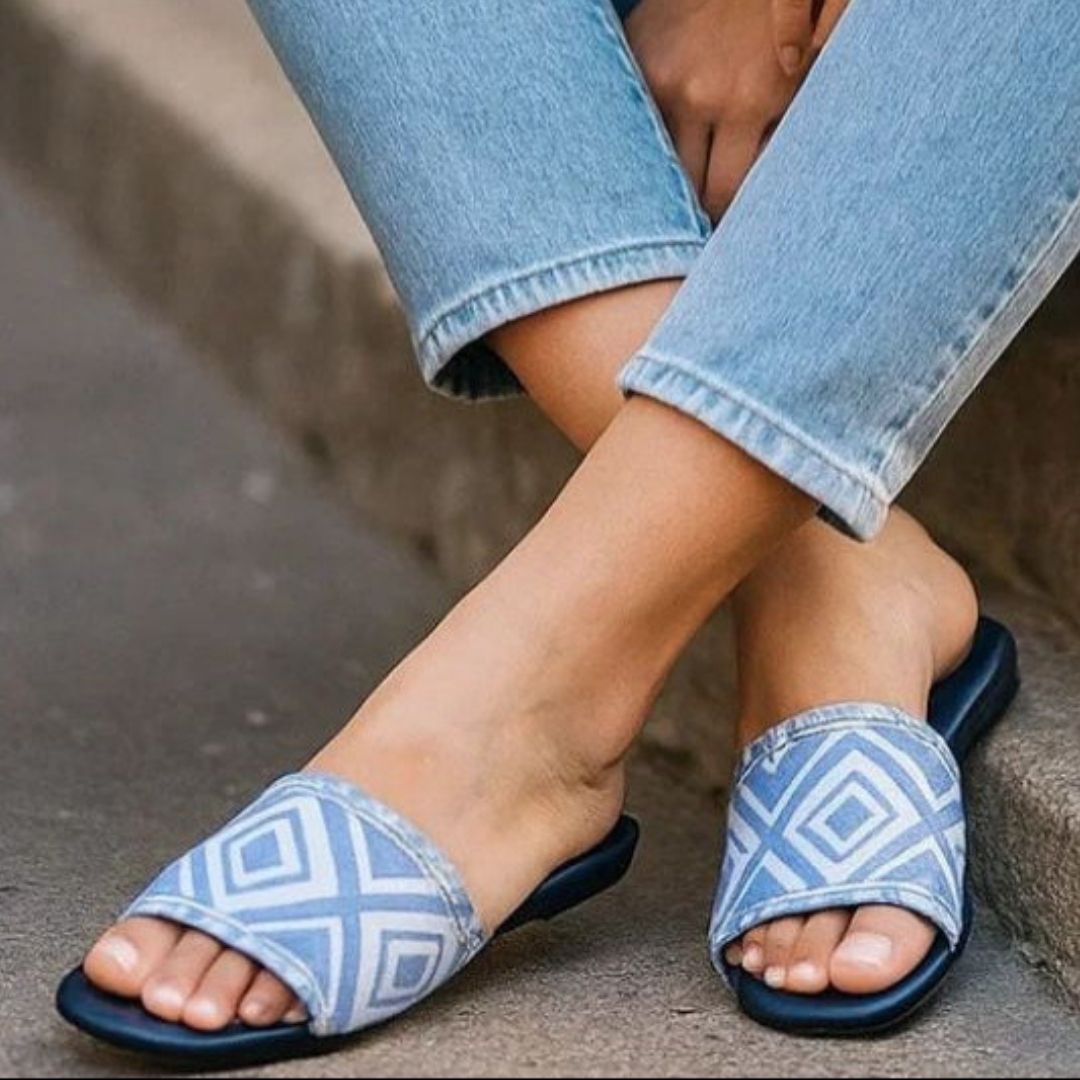 Blue and white patterned sandals worn with rolled-up jeans on a stone surface.