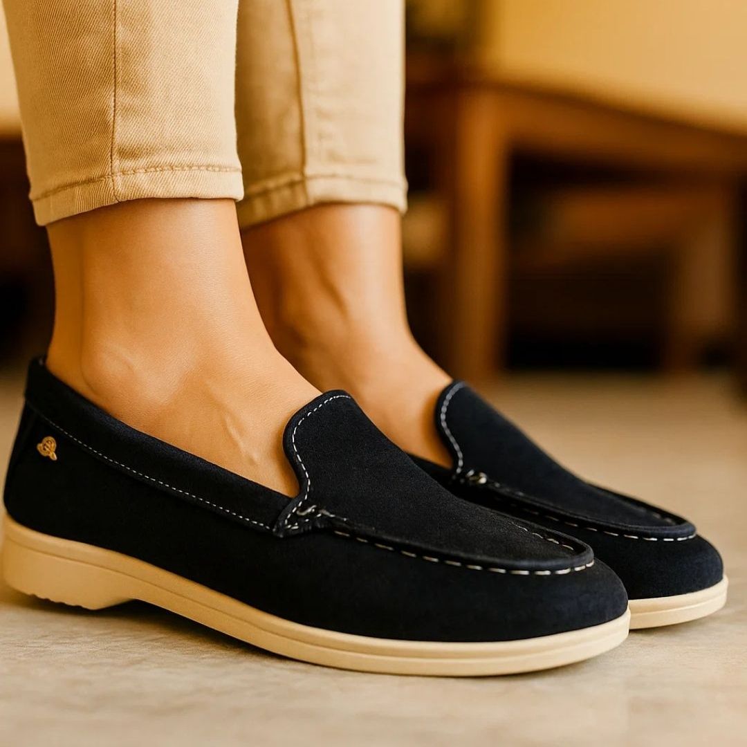 Black loafers worn with beige pants on a blurred indoor background